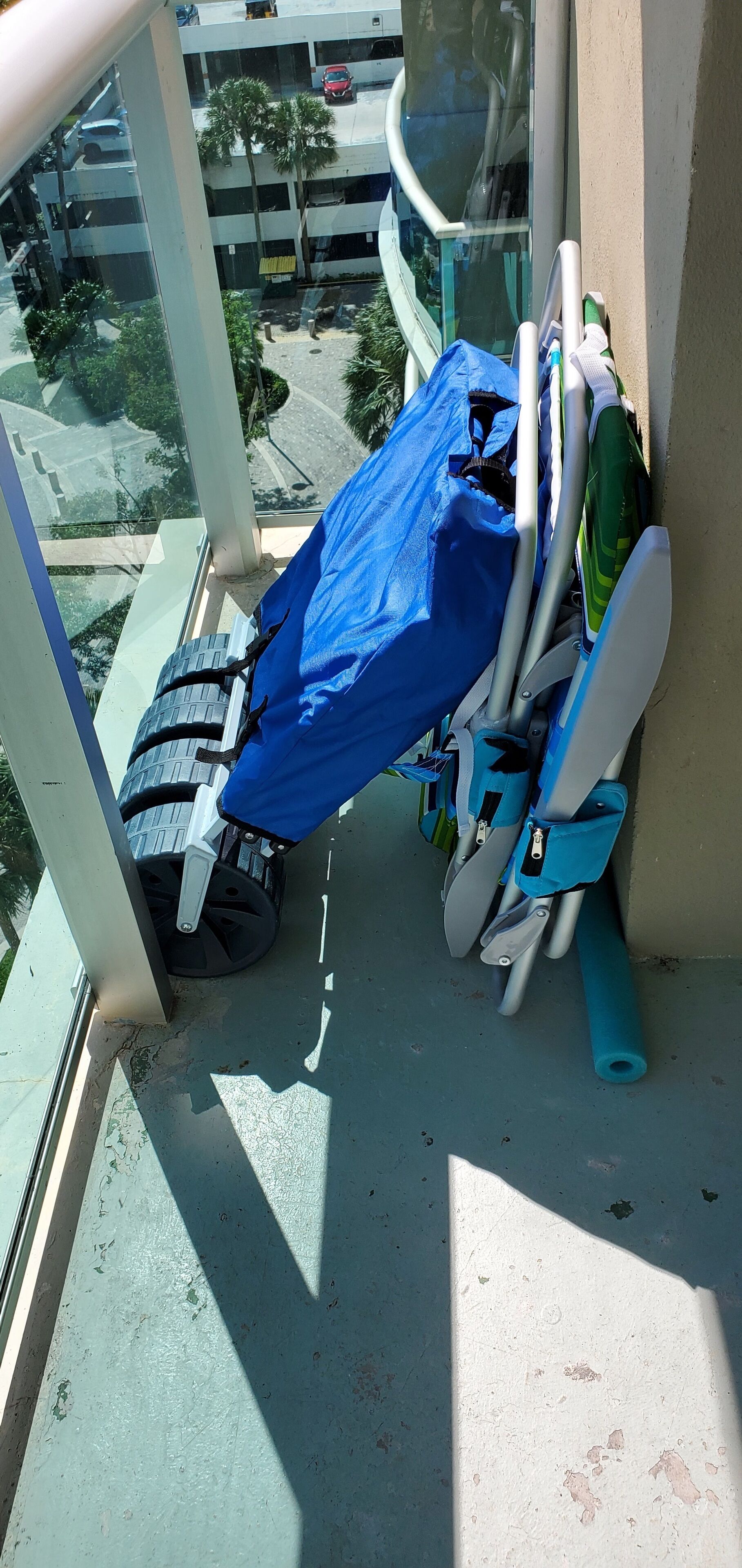 Un balcon avec une bâche bleue recouvrant un scooter, un vélo vert et un tapis bleu.