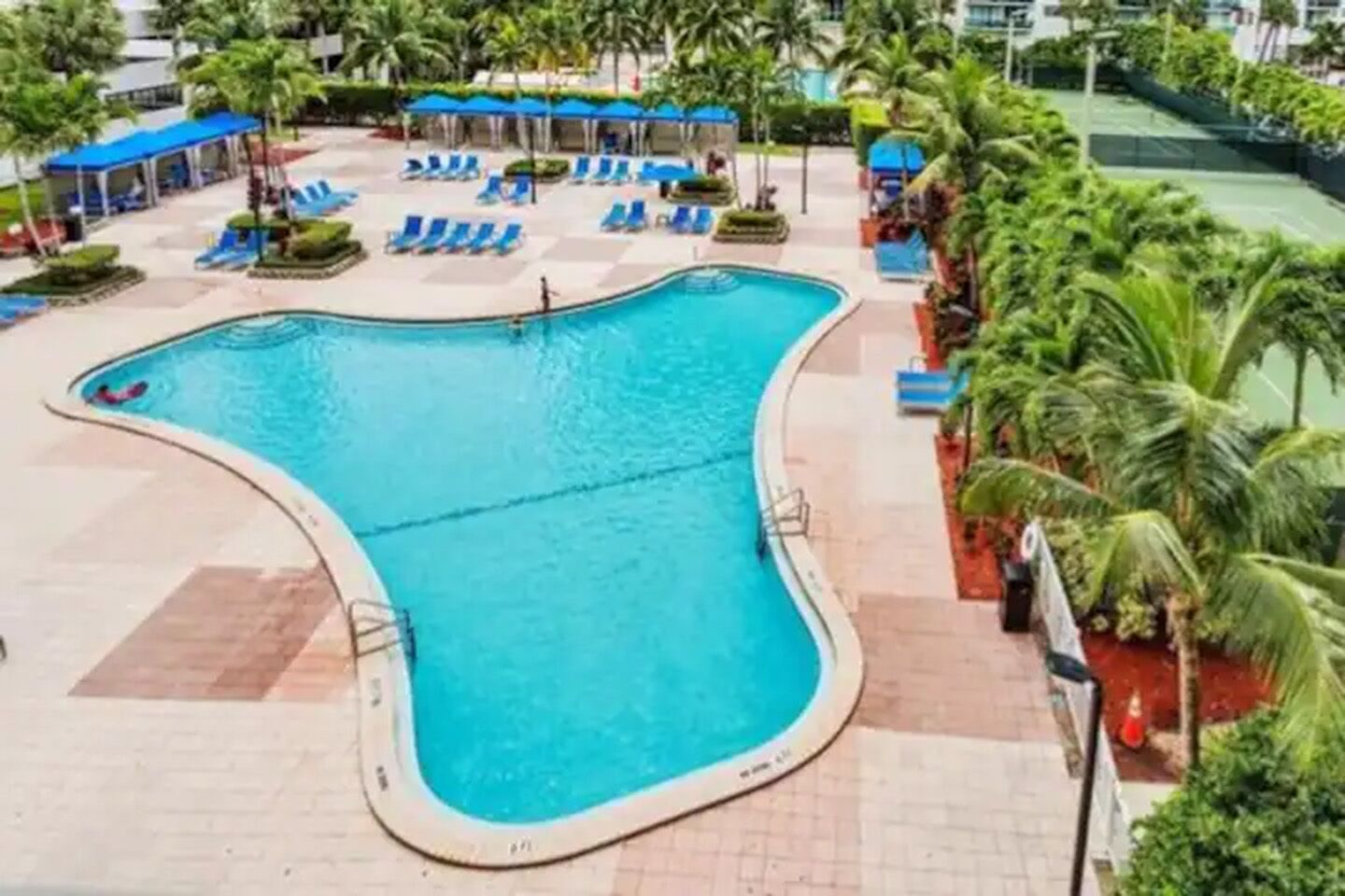 Una piscina con acqua azzurra, circondata da lettini e palme.