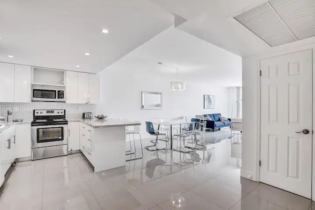 A modern kitchen with white cabinets, a stainless steel stove, and a dining area with a white table and chairs.