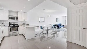 Une cuisine moderne avec des meubles blancs, une cuisinière en acier inoxydable et un coin repas comprenant une table et des chaises blanches.