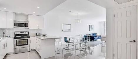 A modern kitchen with white cabinets, a stainless steel stove, and a dining area with a white table and chairs.