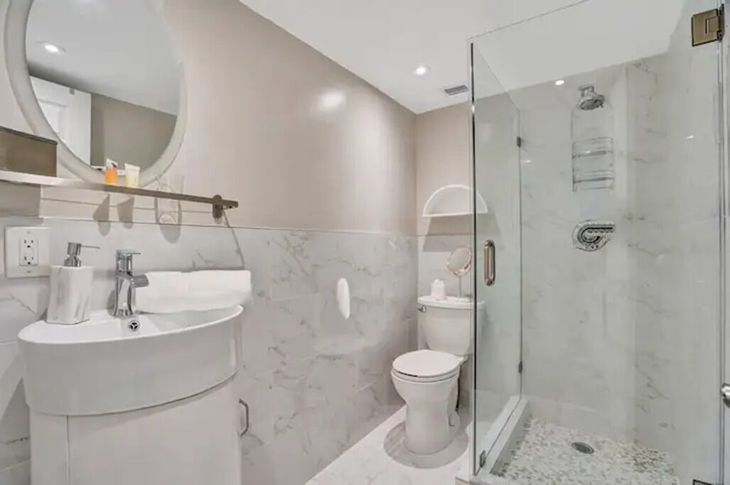 A modern bathroom with a marble sink, toilet, and glass-enclosed shower.
