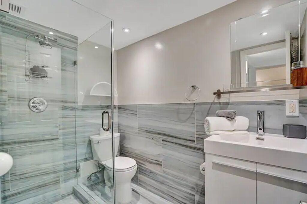 A modern bathroom with a glass-enclosed shower, a white toilet, and a vanity with a mirror.