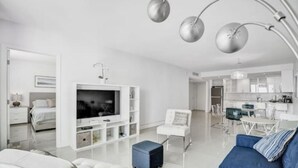 Un salon moderne avec un téléviseur, des meubles blancs et un coin repas.