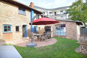 Un patio con mesa y sillas, un paraguas rojo y un edificio de ladrillo con detalles azules.