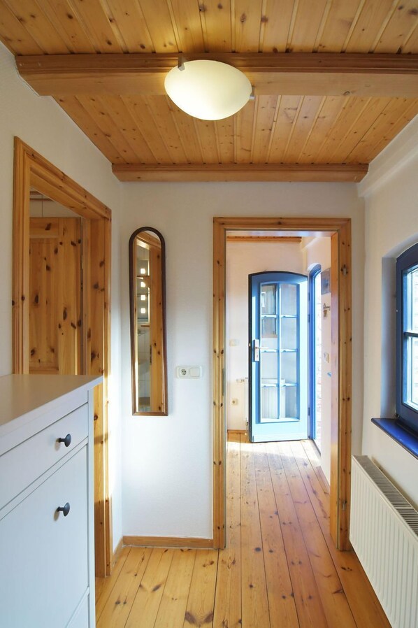 Un pasillo con pisos de madera y techo, un aparador blanco con cajones, un espejo y una puerta que da a otra habitación.