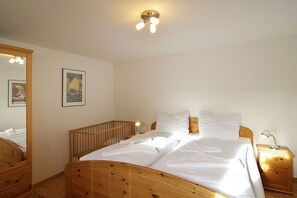 A bedroom with a wooden bed, a nightstand, a mirror, and a wall-mounted light fixture. - Blankenese House - Quaint: Blankenese House on the grounds of Villa Hamburg (Heringsdorf)