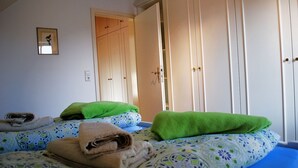 Un dormitorio con dos camas, cada una con una almohada verde y una toalla enrollada. Se observa un armario de madera con un espejo y un cuadro en la pared.