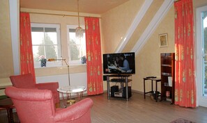 Un salon avec une télévision, des rideaux rouges, un lustre et une bibliothèque.