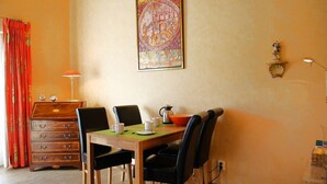 Un comedor con una mesa de madera, sillas negras, una cortina roja, un aparador, un cuadro y una lámpara fijada a la pared.
