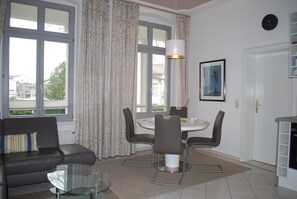 Moderni olohuone, jossa on sohva, lasinen sohvapöytä, ruokapöytä tuoleineen ja riippuvalaisin.