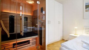 Et moderne soveværelse med sauna i glas, et hvidt garderobeskab og et natbord med lampe.