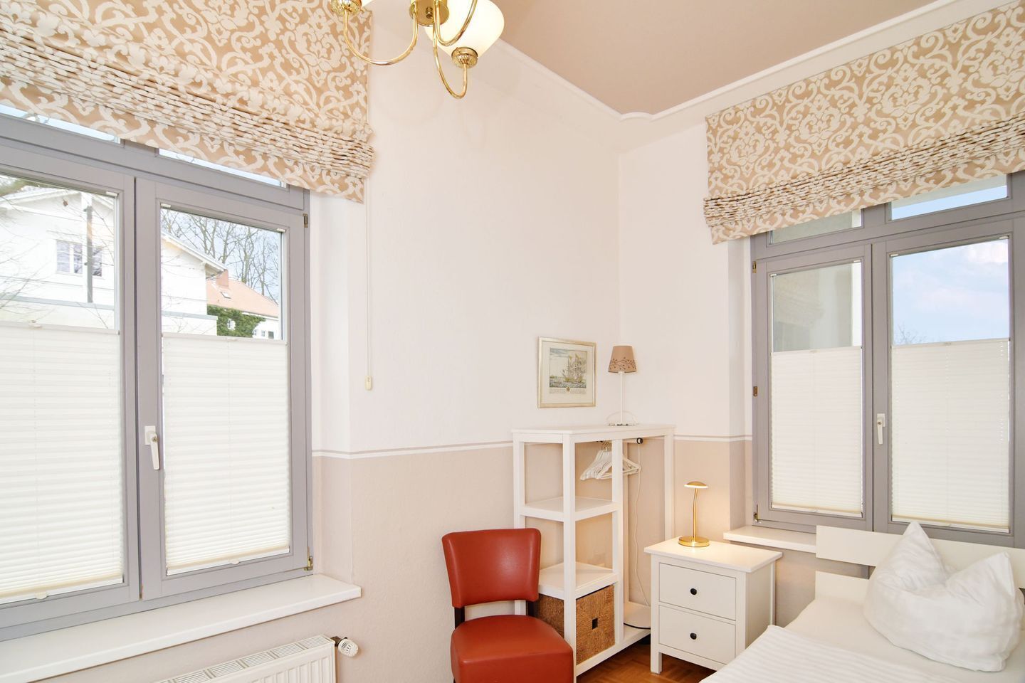 Et soveværelse med to vinduer, en rød stol, et sengebord med en lampe og en seng med en pude.