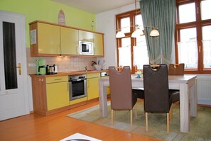 A compact kitchen with yellow cabinets, a microwave, and a stove. There is a dining table with chairs and a window with curtains. - Haus Bellevue Appartement 14 - Haus Bellevue (Heringsdorf)