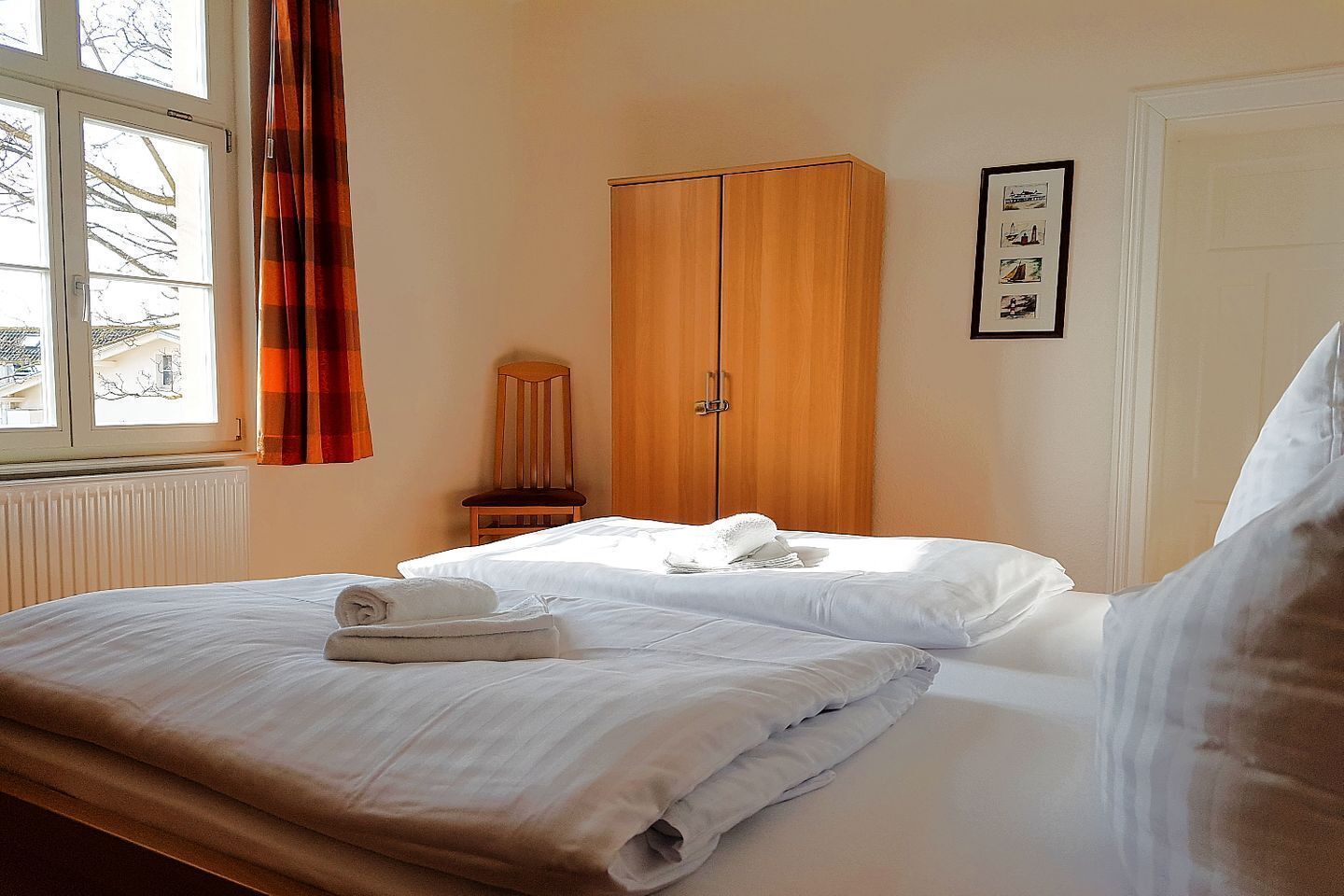 A hotel room with a bed, a wooden wardrobe, a chair, and a window with curtains.