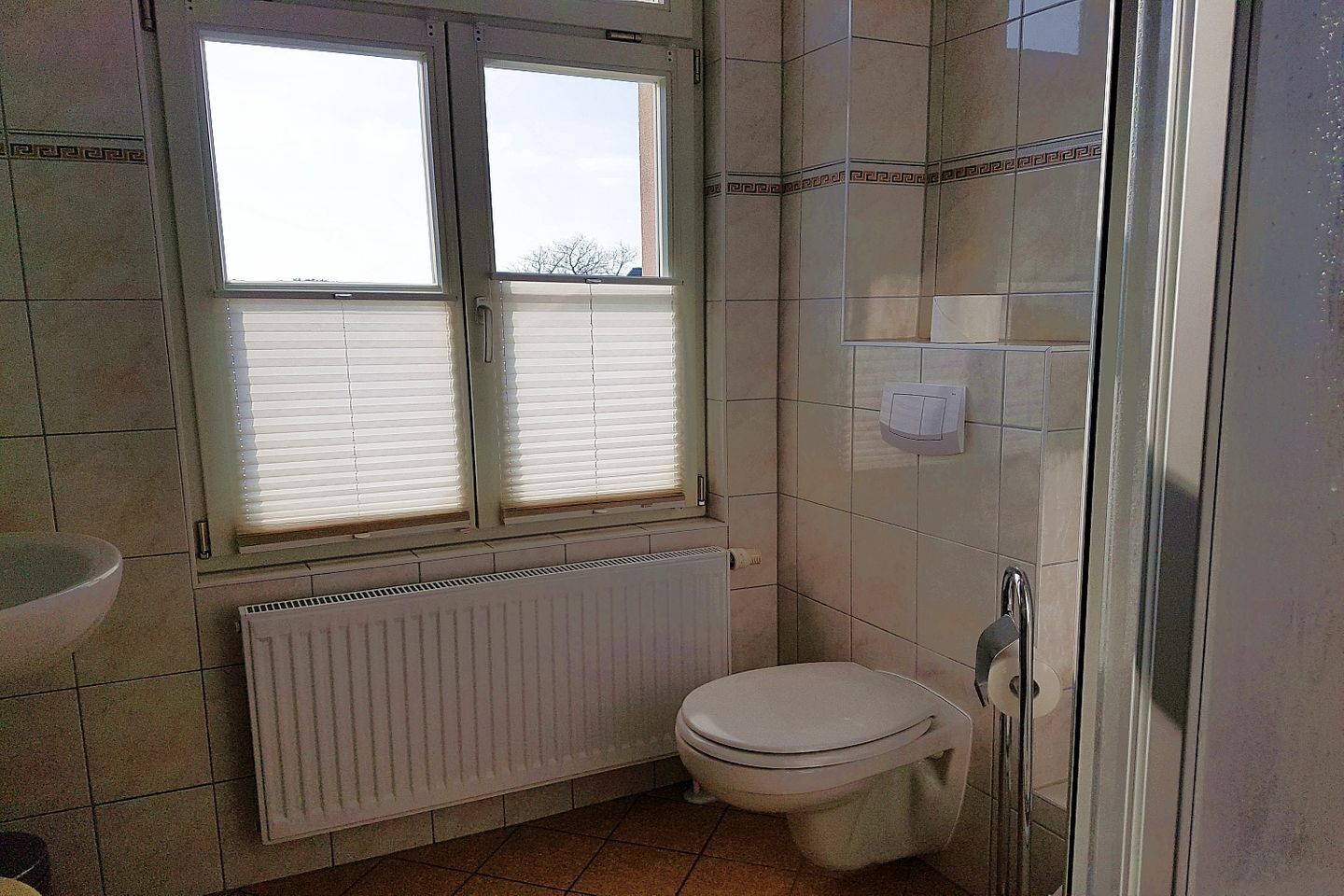 A bathroom with a toilet, a window with blinds, a shower area, and a radiator.