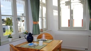 Ein Essbereich mit Holztisch, zwei Stühlen, einer blauen Karaffe und einem Fenster mit Vorhängen.