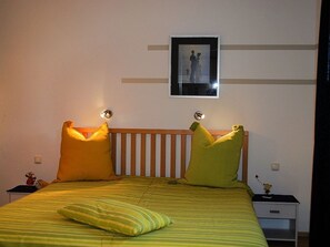 A bed with green and yellow striped bedding, two pillows, a wooden headboard, a nightstand with a clock, and a framed picture on the wall. - Haus Bellevue Wohnung 10 - Haus Bellevue (Heringsdorf)