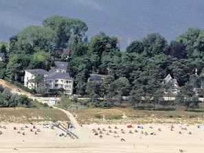 Una playa con varias sombrillas y tumbonas. Se observan varias casas al fondo, rodeadas de árboles.