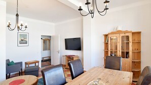 Un comedor con mesa de madera, sillas de cuero, una lámpara de araña, televisor y aparador de madera.