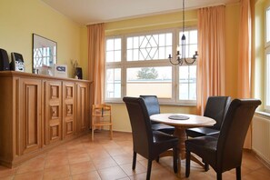 Uma sala de jantar com uma mesa redonda e quatro cadeiras, um armário de madeira e uma janela com cortinas.