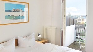 Une chambre d’hôtel avec un grand lit, une table de chevet avec une lampe, un tableau encadré au mur et un balcon avec une chaise.