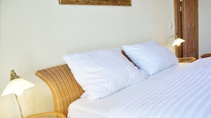 Una cama bien hecha con sábanas blancas, dos lámparas de noche y un cabecero de mimbre.