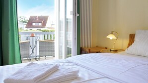 Habitación de hotel con cama, mesita de noche, lámpara, sillón y vistas al exterior.