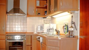 Een kleine keuken met houten kastjes, een inbouwoven, een koffiezetapparaat en een spoelbak met kraan.