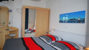 Een slaapkamer met een bed, een bureau, een stoel, een spiegel en een schilderij van een brug.
