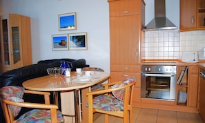 Cocina compacta con armarios de madera, horno integrado y comedor con mesa redonda y dos sillas.