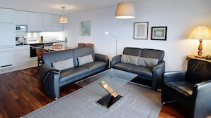 A modern living room with a sofa set, a coffee table, and a dining area with a kitchen in the background.