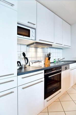 A modern kitchen with white cabinetry, a built-in microwave, a stove, and a sink.