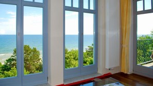 A room with large windows overlooking a coastal view, a white radiator, and a red support beam.