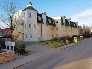 A multi-story residential building with a central tower, a green roof, and a paved driveway.