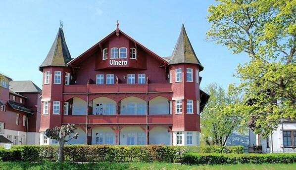 A red building with the name "Vineta" on the facade, featuring a symmetrical design with two towers and a central section with multiple windows. - Villa Vineta Appartement 15 - Villa Vineta (Heringsdorf)