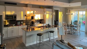 Une cuisine moderne avec des meubles blancs, un îlot central doté de tabourets, un four à micro-ondes et une cuisinière.