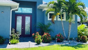 A modern house with a blue exterior, a purple front door, and a well-maintained garden with palm trees and flowering plants. - 15 min. from the beaches, one-of-a-kind, Villa Philippa, modern, south-facing with a view of the canal,  (Rotonda West)