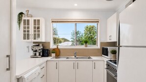 A modern kitchen with white cabinetry, a built-in oven, a microwave, and a window with a view of trees.