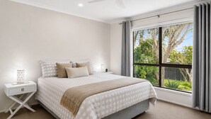 A bedroom with a bed, nightstands, a ceiling fan, and a large window with curtains.