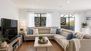A modern living room with a sectional sofa, a flat-screen TV, a coffee table, and a small cabinet.