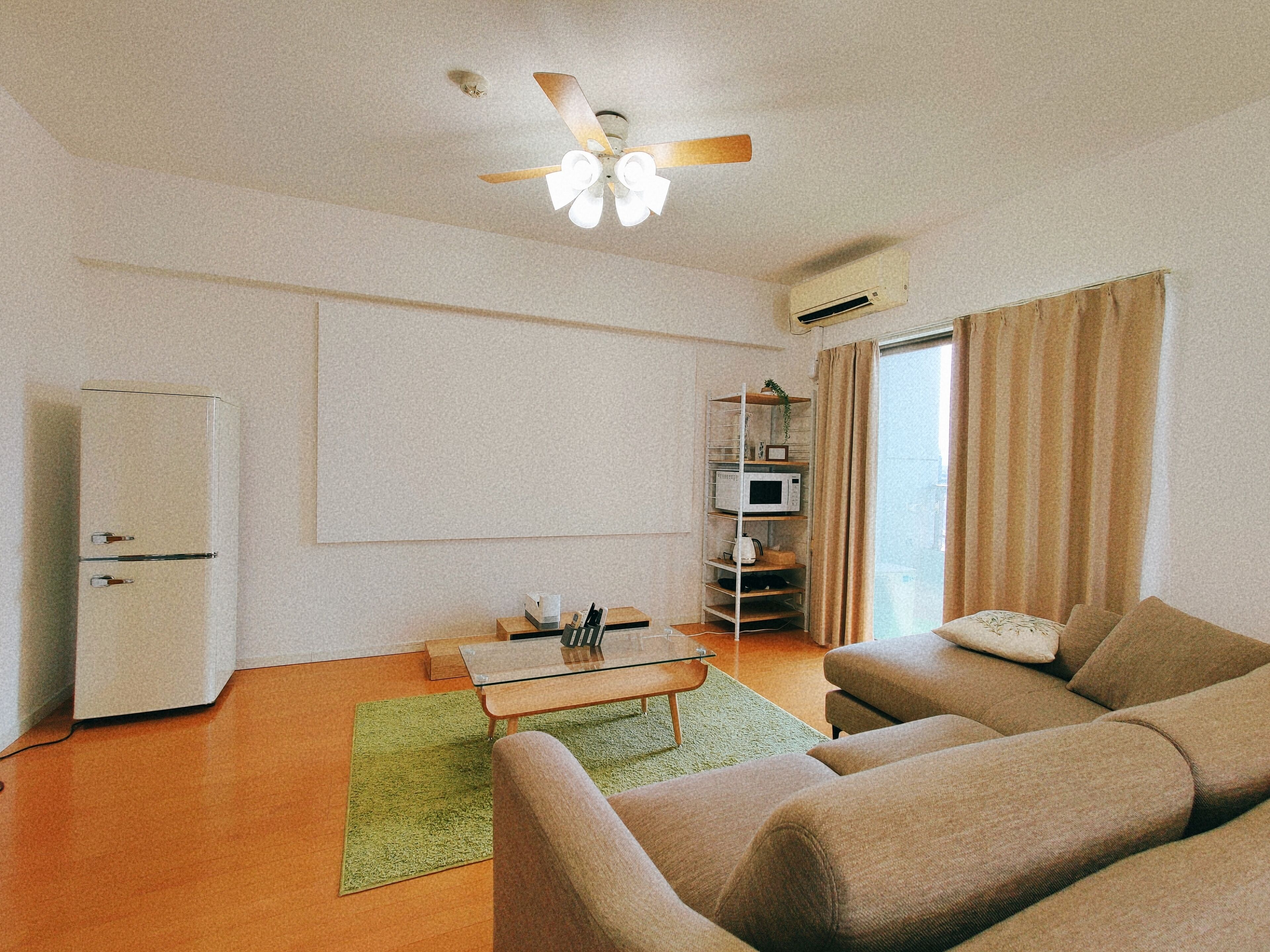 A compact living space with a ceiling fan, a microwave on a shelf, a sofa, and a small table.