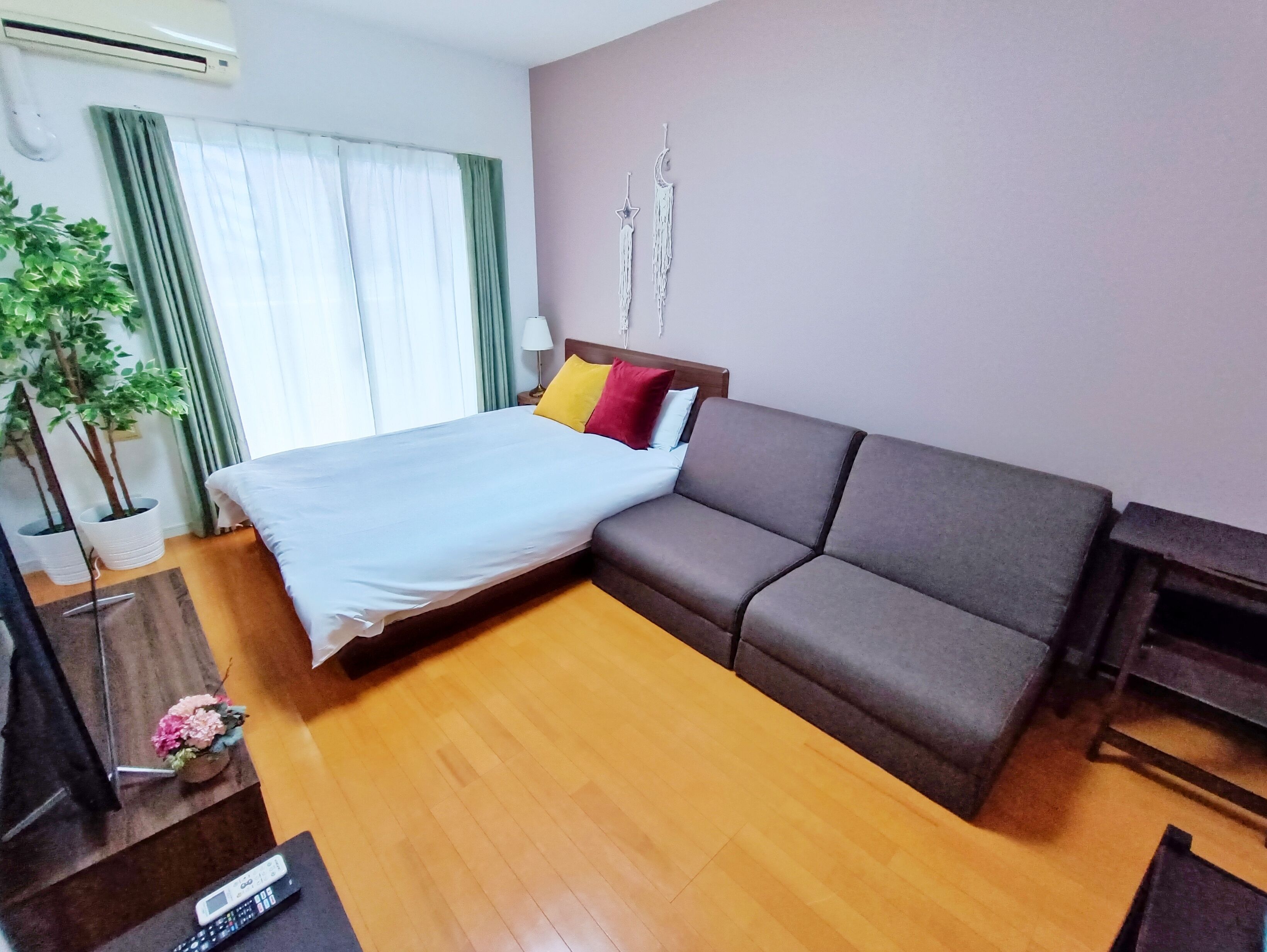 Ein Hotelzimmer mit einem Bett, einer Couch, Holzboden, einer Topfpflanze und einer Lampe.