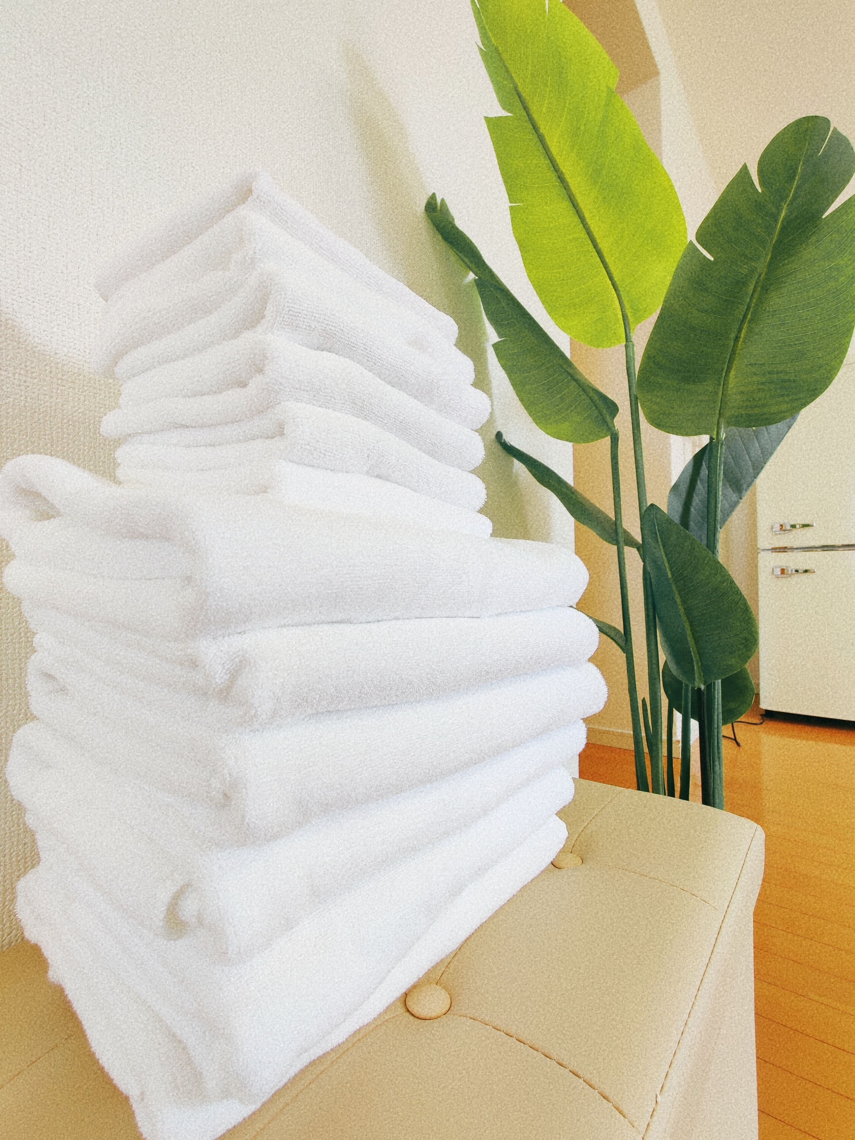 A stack of white towels on a beige chair with a green plant beside it.