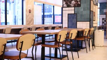 A restaurant interior with wooden tables and chairs, large windows, and a tiled wall with hexagonal patterns.