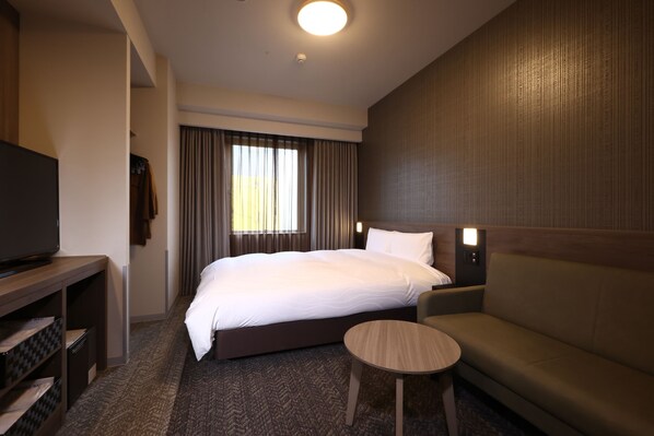 A hotel room with a large bed, a small round table, a sofa, a TV, and a window with curtains.