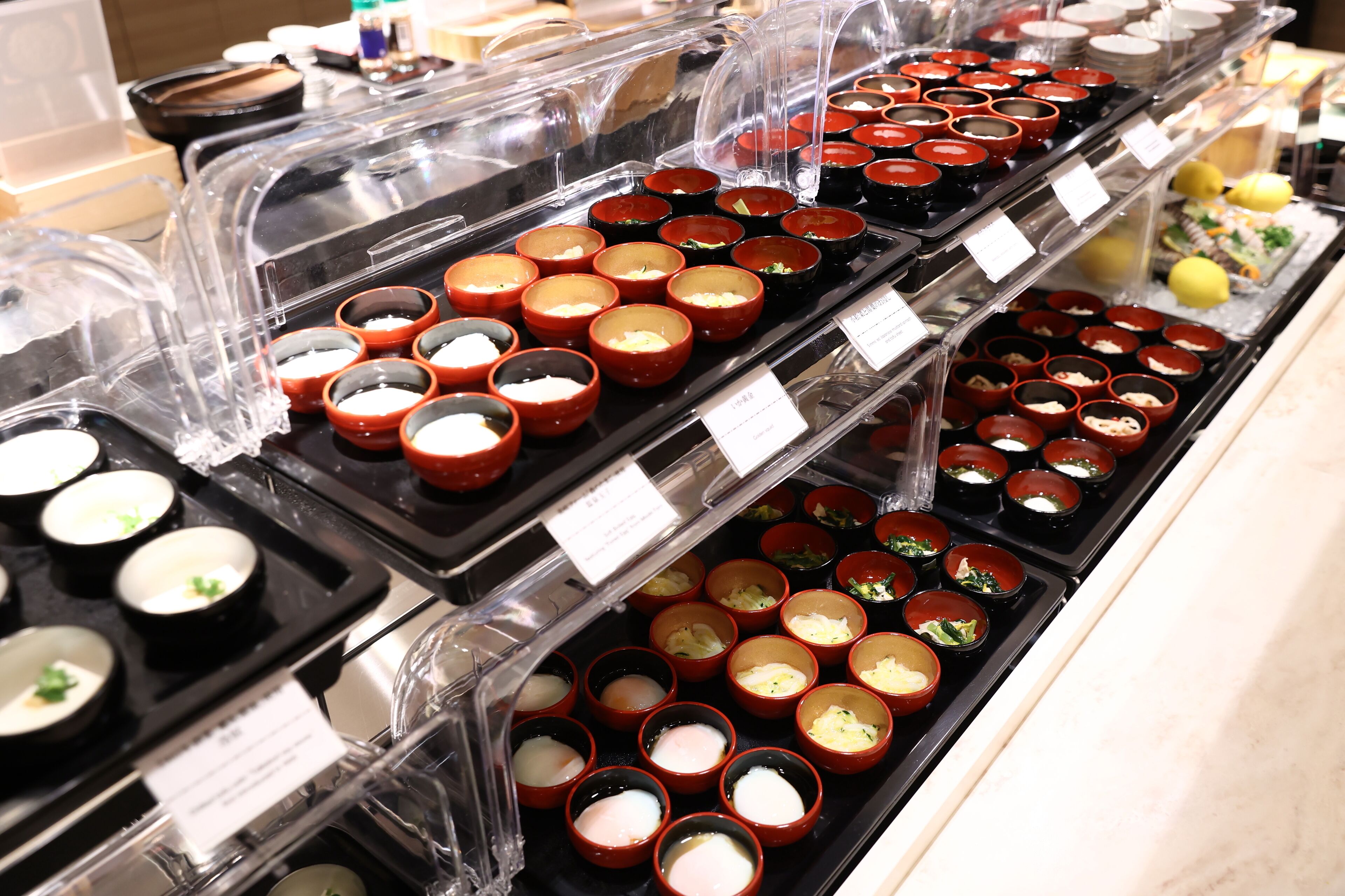 Un bufé con diversos platos en recipientes pequeños, dispuestos en bandejas.