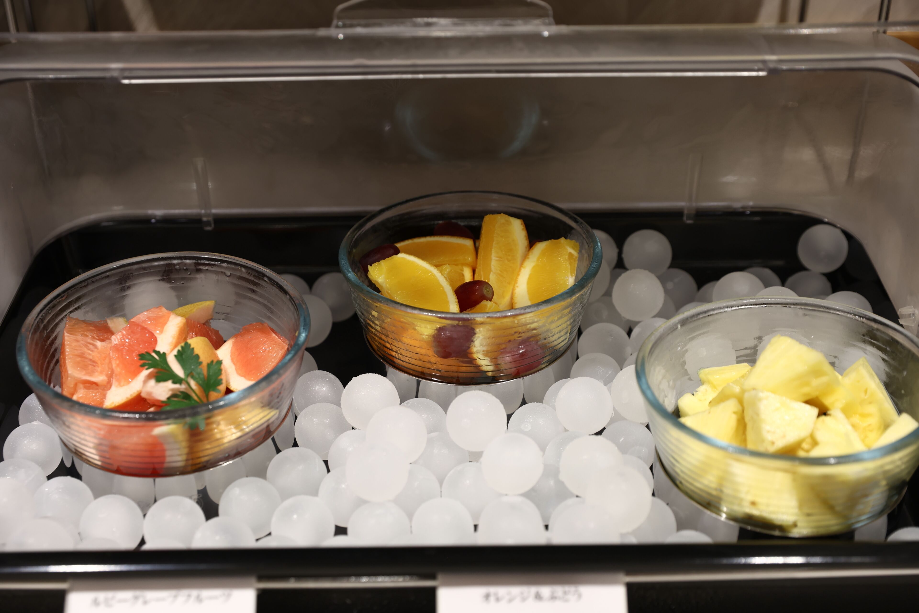 Three glass bowls containing different fruits on ice cubes in a refrigerated display.