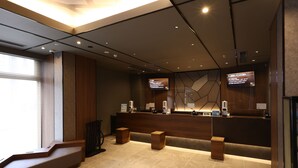 A modern reception area with a wooden reception desk, a digital display, and a seating area with wooden stools. - Dormy Inn Okayama (Okayama)