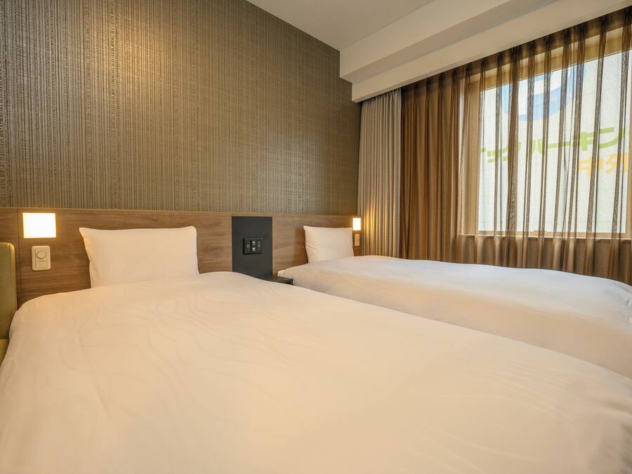 Habitación de hotel con dos camas, cabecera de madera, mesita de noche y ventana con cortinas.